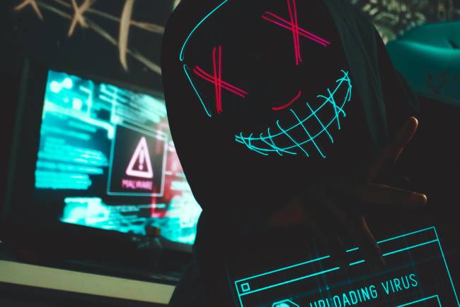 Eine neue Rust-Malware namens ChaosBot nutzt Discord als Kommandozentrale. das soll hier ein verkleideter Hacker mit einem bildschirm auf dem ein Warnzeichen zu sehen ist symbolisieren. Bild: Pexels/Lucas Andrade
