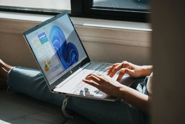 Windows 11 25H2 bringt Stabilität, Performance und moderne KI-Funktionen für Unternehmen das soll hier eine Frau die vor ihrem Windows Microsoft Laptop sitzt verdeutlichen. Bild: Unsplash/Windows